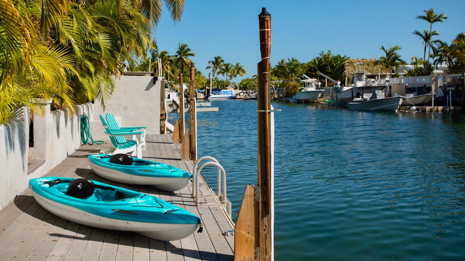 Two kayaks on a dock at a waterfront Key West vacation rental. Palm trees and boats are visible in the background.